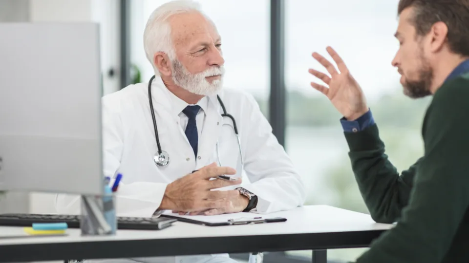 Médico de jaleco conversando com um paciente durante consulta em consultório