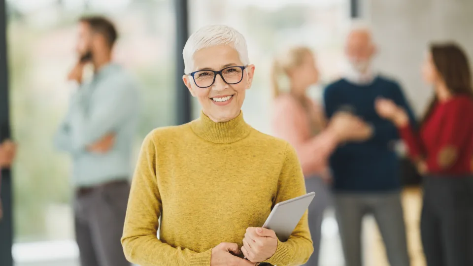Mulher madura de cabelos grisalhos e óculos, sorrindo em ambiente de trabalho