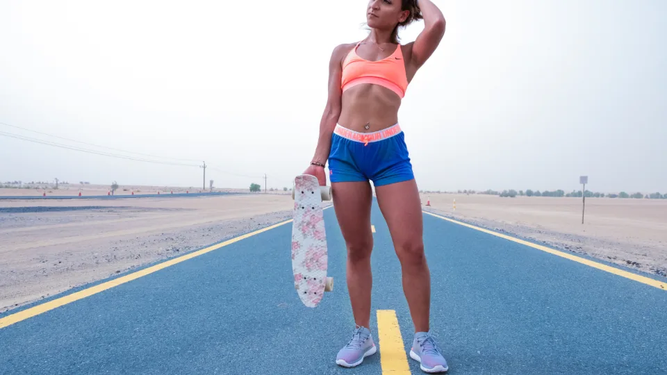 Mulher em roupa de treino segurando um skate em uma via ao ar livre