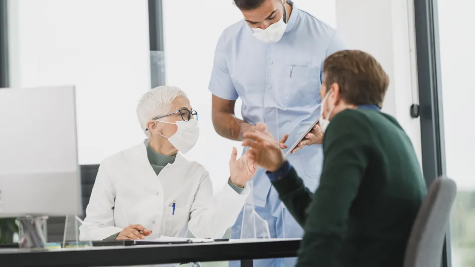 Equipe de saúde de máscara atendendo uma paciente em ambiente clínico